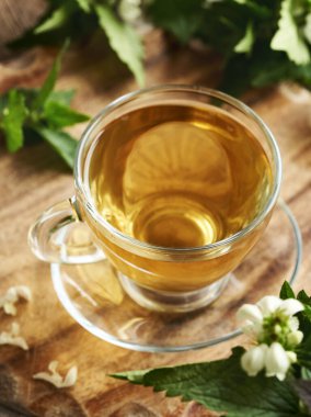 Taze beyaz ısırgan otu çiçekleri ve yaprakları olan bir bardak bitki çayı.