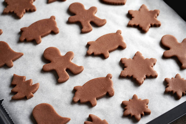 Shapes cut out from raw pastry dough on a baking sheet - preparation of homemade gingerbread Christmas cookies