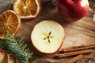 Ortası tarçınlı, kurutulmuş portakal dilimli ve Noel süslemeli yarım bir elma.