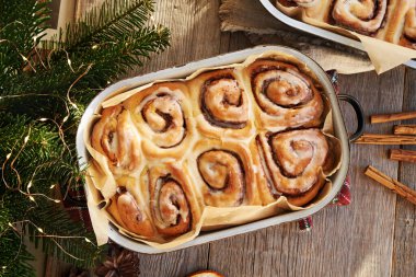 Ev yapımı tarçınlı çörekler, içinde Noel ağacı dalları olan fırın tepsisi.