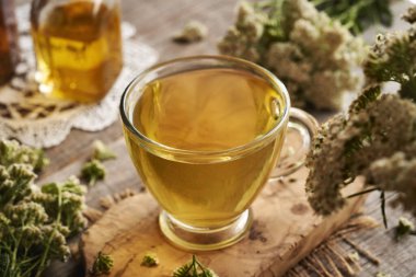 Şeffaf cam bir fincanda taze kireçli bitki çayı ya da ahşap bir masada Achillea Millefolium çiçekleri.