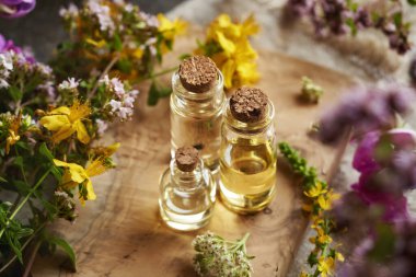 Üç şeffaf aromaterapi şişesi ahşap bir masanın üzerinde renkli yaz çiçekleri olan gerekli yağ.