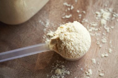 Tahta bir masada ölçü kabında beyaz protein tozu.