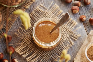 Homemade hazelnut butter in a glass jar with a spoon, top view clipart