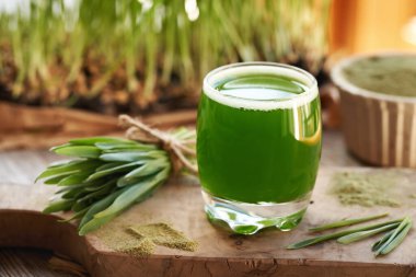 Bir bardak yeşil arpa tohumu suyu ve ahşap bir masada taze yetiştirilmiş bıçaklar.