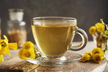 Bir bardak çaydanlık çayı ve masada da taze tay çiçeği.