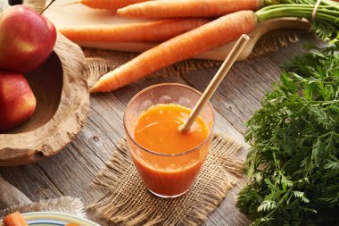 Bir bardak taze havuç suyu, ekolojik bambu pipetli ve kırmızı elmalı.