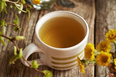 Kırsal ahşap bir masanın üzerinde taze kokarca ayaklı bir fincan çay.