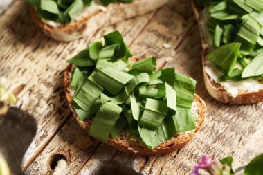 Tahta masadaki bir dilim ekmeğin üzerinde yabani sarımsak yaprakları.