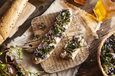 Taze sarmaşık çiçekleri ve baharda toplanan yapraklar ahşap bir masanın üstünde ekmek rulosu, üst manzara