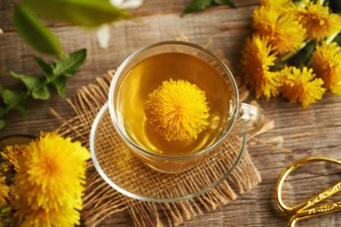 İlkbaharda toplanan karahindiba çiçeği ahşap bir masada bir fincan bitki çayında toplanır.