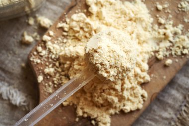 Şeffaf bir plastiğin içindeki beyaz protein tozu bir masanın üzerindeki kepçeyi ölçer.