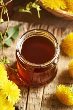 Masada taze karahindiba çiçekleri olan cam bir karahindiba kavanozu.