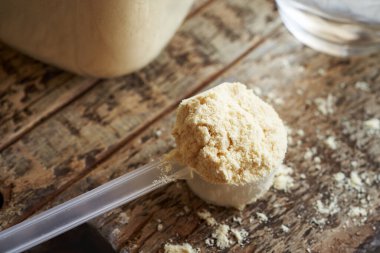 Tahta bir masada şeffaf bir kaşık içinde beyaz protein tozu.