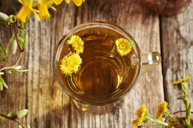 Tahta bir masada, bir fincan bitki çayının içindeki Coltsfoot çiçekleri.