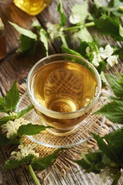 Şeffaf cam bir fincan bitkisel çay ve masada taze taze, ölü ısırgan otu tohumu. Alternatif tıp.