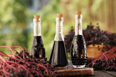 Güneşli bir yaz gününde üç şişe siyah yaşlı şurubu ve açık havada taze elderberry.