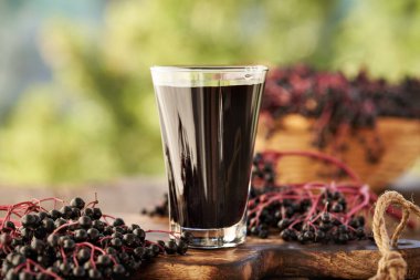 Bir bardak siyah yaşlı şurubu ve açık bir masada taze elderberry.