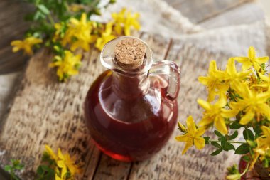 Masanın üzerinde taze Hypericum çiçekleri olan bir şişe St.John otu yağı.