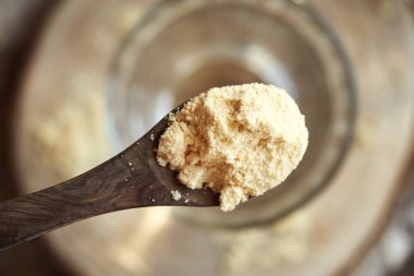 Tahta bir kaşıkta beyaz protein tozu, bir bardak suyun üstünde, üst manzara.