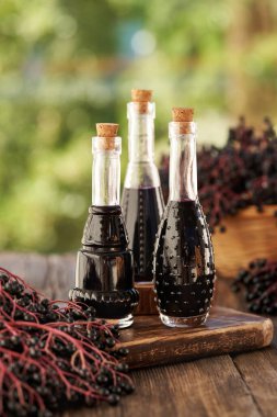 Yazın açık bir masada taze elderberry ile üç şişe siyah yaşlı şurubu.