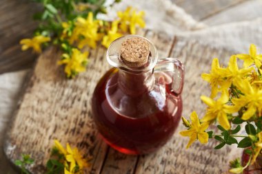 Kırmızı St. John 's marihuana yağı cam bir şişede ve masada taze çiçekler