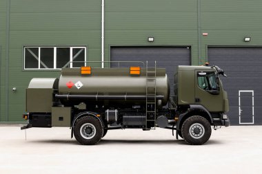 Bir hangarın arka planında askeri teçhizat, bir haki dizel teknoloji tankeri.