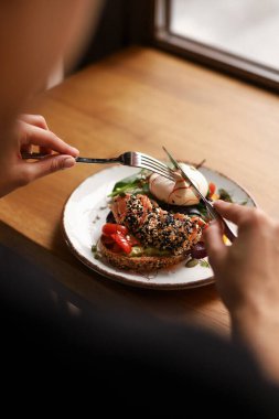 Kahverengi bir tabakta kızarmış ekmek sandviç, guacamole, kırmızı balık, yumurta ve yeşillikler.