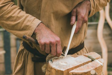 Elleri ve bir odun parçası üzerinde bıçakla çalışan bir zanaatkar.