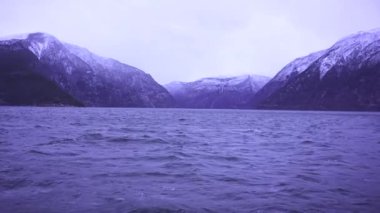 Karlı dağ zirveleri, sakin kış manzarası ve Norveç 'teki gri bulutlu gökyüzü ile buzlu bir fiyordun yakın görüntüsü