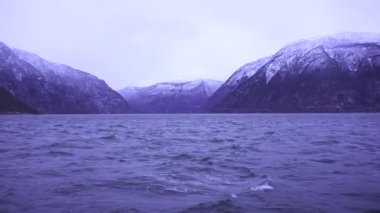 Soğuk dalgalı su, karla kaplı dağlar ve hafif bir hareketle yakalanmış barışçıl bir atmosfer ile kışın sakin bir Norveç fiyordu..