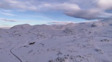 Norveç 'te, engin karlı bir plato, engebeli dağ zirveleri ve dramatik bulutlu gökyüzünün yer aldığı çarpıcı bir kış ormanı. Kuzey Kutbu 'nun sakin manzarası huzur veriyor, dokunulmamış güzellik.
