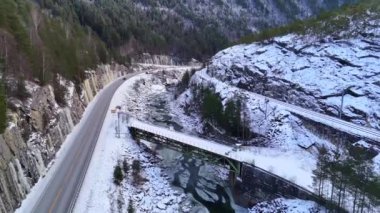 Norveç 'te karlı bir vadiyi gösteren nefes kesici bir kış manzarası. Köprüsü, donmuş nehri, manzaralı yolu ve ormanlı dağları olan bir vadi.