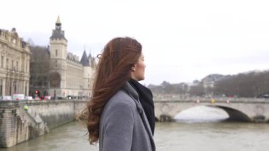 Paris köprüsünde zarif poz veren sofistike bir kadın, tarihi mimari ve romantik şehir atmosferi tarafından çerçevelenmiş.