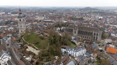 Drone view over Mons, Belgium, featuring the UNESCO-listed belfry, Saint Waltrude Collegiate Church, historic rooftops, and green spaces in the medieval city center. clipart