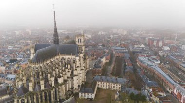 Amiens, Fransa 'daki ikonik Gotik katedralin hava görüntüsü, sisli ve bulutlu bir gökyüzü altında şehir manzarasıyla çevrili.. 
