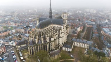 Fransa 'nın kuzeyindeki Gotik Amiens Katedrali' nin sisli bir gökyüzünün altındaki şehir manzarasıyla çevrili hava manzarası.
