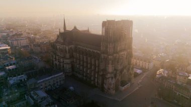 Aerial view of Reims Cathedral during sunrise, bathed in golden light. The Gothic landmark overlooks the historic cityscape of Reims, France, in a serene atmosphere. clipart