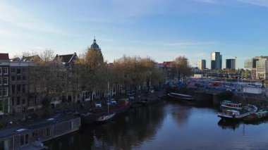 Altın saat boyunca bir Amsterdam kanalının çarpıcı hava manzarası, demirli tekneler ve sıcak güneş ışığı suya yansıyor..