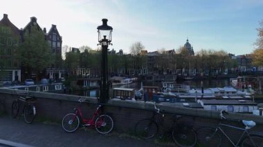 Amsterdam nehrinin manzaralı günbatımı manzarası, park halindeki bisikletler ve suyun üzerinde parlayan gökyüzü yansımaları..