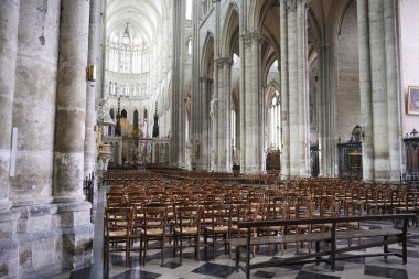Geniş katedral iç mekânında ahşap sandalyeler, gotik kemerler ve arka planda çarpıcı vitray pencereler yer alıyor..