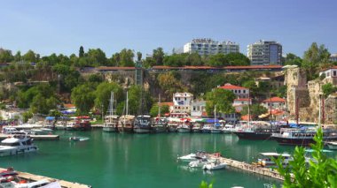 Antalya, Türkiye 11.02.2024 Turkuvaz suları, renkli tekneler, yemyeşil, tarihi binalar ve canlı bir kıyı atmosferinin yer aldığı Eski Kent marinasının manzarası.