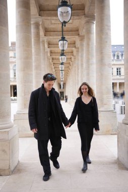 Siyahlar içinde şık bir çift Paris 'teki Palais-Royal' in büyük sütununda el ele yürür. Romantizm, zerafet ve zamansız Fransız modası yayarlar..