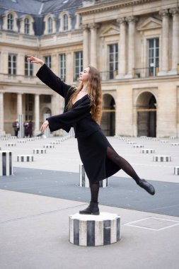 Siyah elbiseli şık bir kadın Paris 'teki Palais-Royal' de çizgili bir sütunda zarif bir şekilde dengede duruyor. Tarihi mimarinin ortasında baleden esinlenerek poz veriyor..