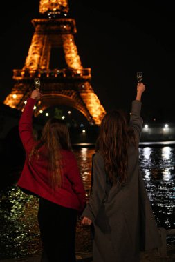 İki arkadaş Eyfel Kulesi 'nin önünde kadehlerini kaldırarak, neşeyle hayatı kutluyorlar.