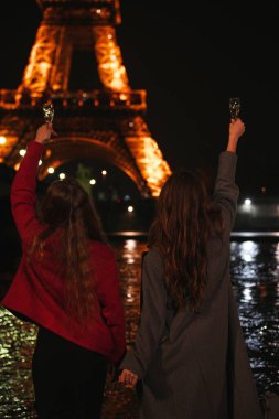 Kutlama için kadehlerini kaldıran iki arkadaş, Eyfel Kulesi 'nin ikonik ışıklarıyla güzel bir şekilde aydınlatılıyor.
