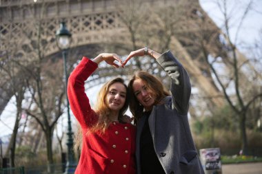 İki mutlu arkadaş Eyfel Kulesi 'nin önünde poz veriyor. Elleriyle bir kalp şekli oluşturuyor. Paris' te aşkı, dostluğu ve neşeyi simgeliyor..