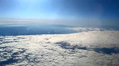 Yüksek irtifada bir hava manzarası gökyüzü boyunca uzanan geniş bir kalın bulut tabakasını ve aşağıdaki kara parçalarını gösteriyor.. 