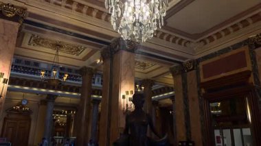 03.18.2025 Monaco, Fransa, gözleri bağlı bir kadının çarpıcı bronz heykeli mermer sütunlar, avizeler ve karmaşık mimari detaylarla süslenmiş büyük bir salonda duruyor..