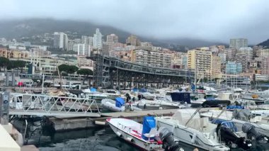 03.18.2025 Monaco, Fransa, bulutlu bir gökyüzü altında modern yaya köprüsü ve yüksek binaların yer aldığı tekne ve yatlarla dolu bir marina manzarası